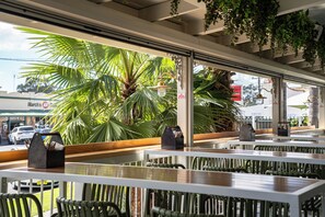 An outdoor cafe with tables and chairs, a view of palm trees, and a 'No Smoking' sign.