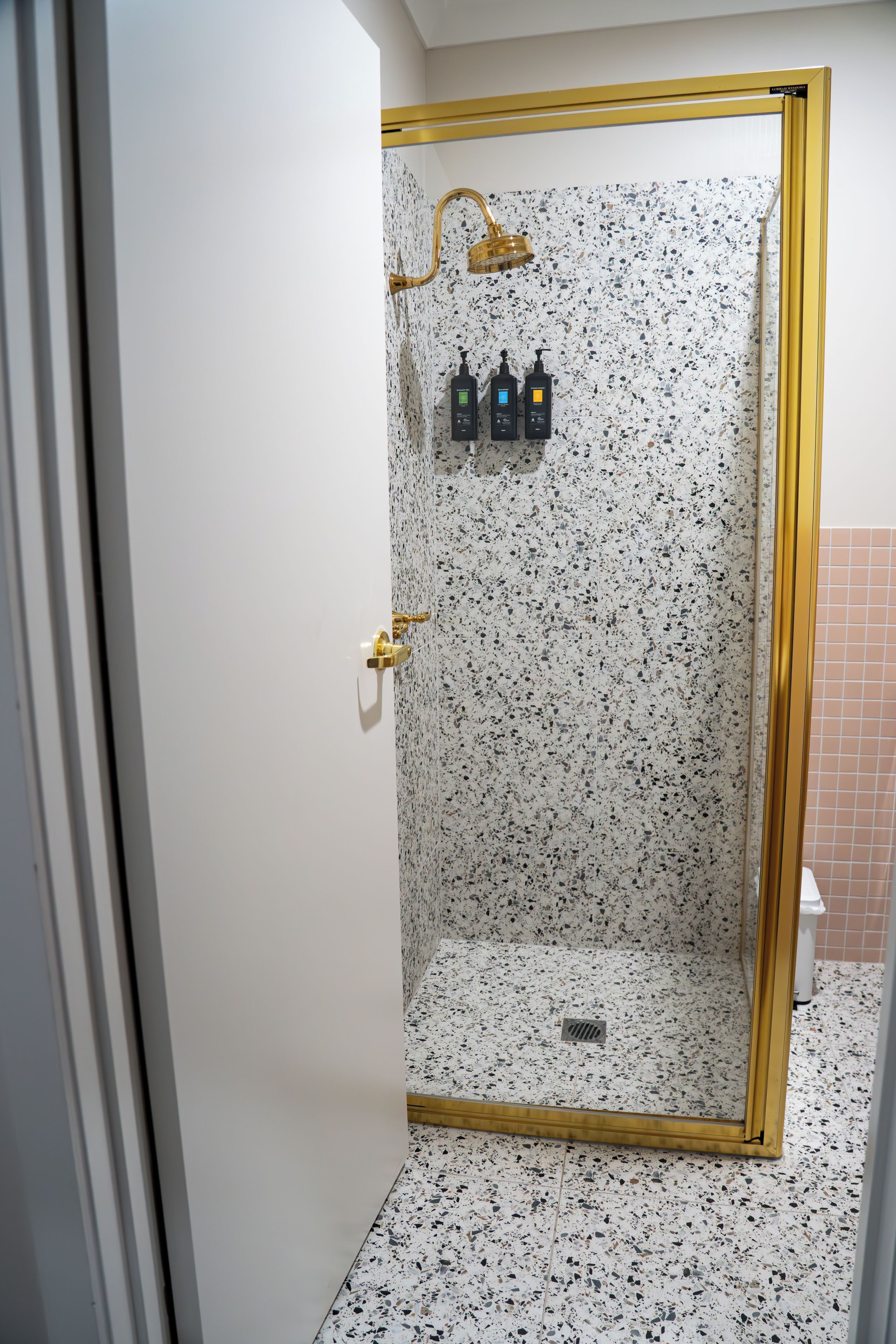 A walk-in shower with a speckled tile floor and a gold-framed glass door.