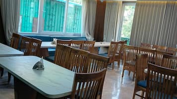 Un comedor con mesas y sillas de madera, ventanas amplias con cortinas e iluminación empotrada en el techo.