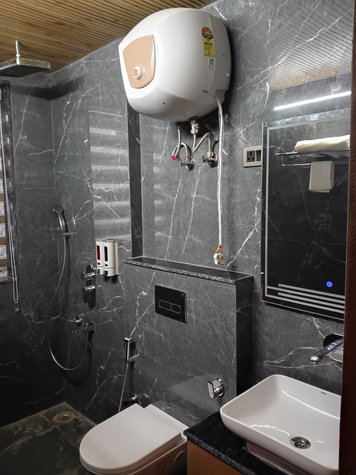 Un bagno con una parete in marmo, un WC bianco, un lavandino e una doccia con soffione a mano.