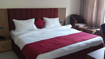 Una habitación de hotel con una cama grande, cabecera, mesita de noche, una silla y un ventilador de techo.