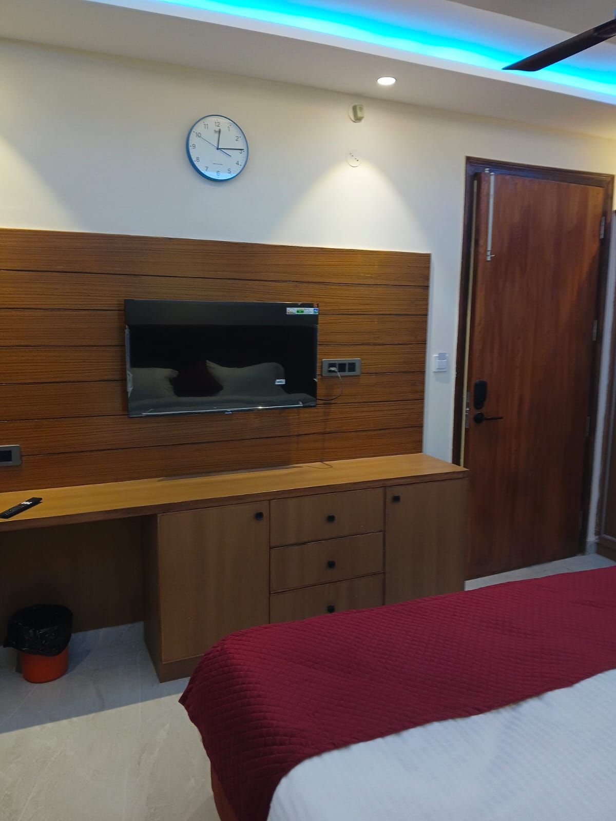 Un dormitorio con una cama, un aparador de madera, un televisor montado en la pared y una puerta.