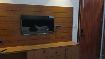 Un dormitorio con una cama, un aparador de madera, un televisor montado en la pared y una puerta.