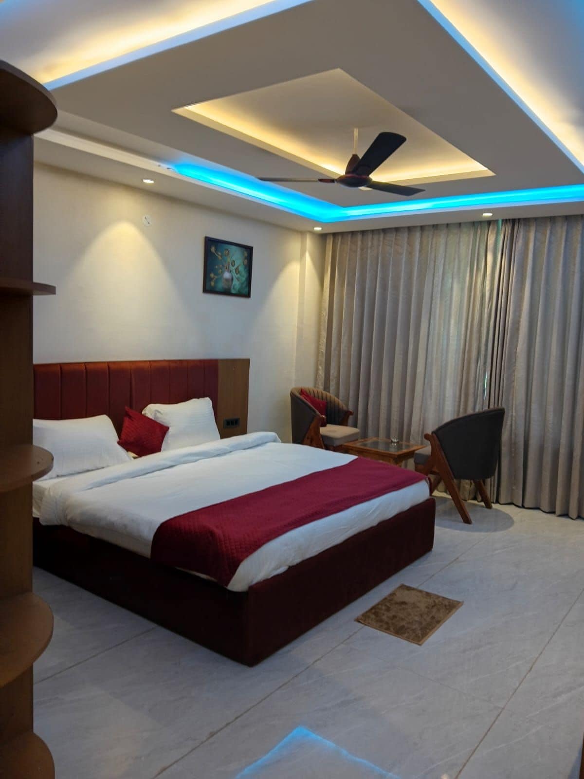 A modern hotel room with a large bed, a ceiling fan, and a painting on the wall.