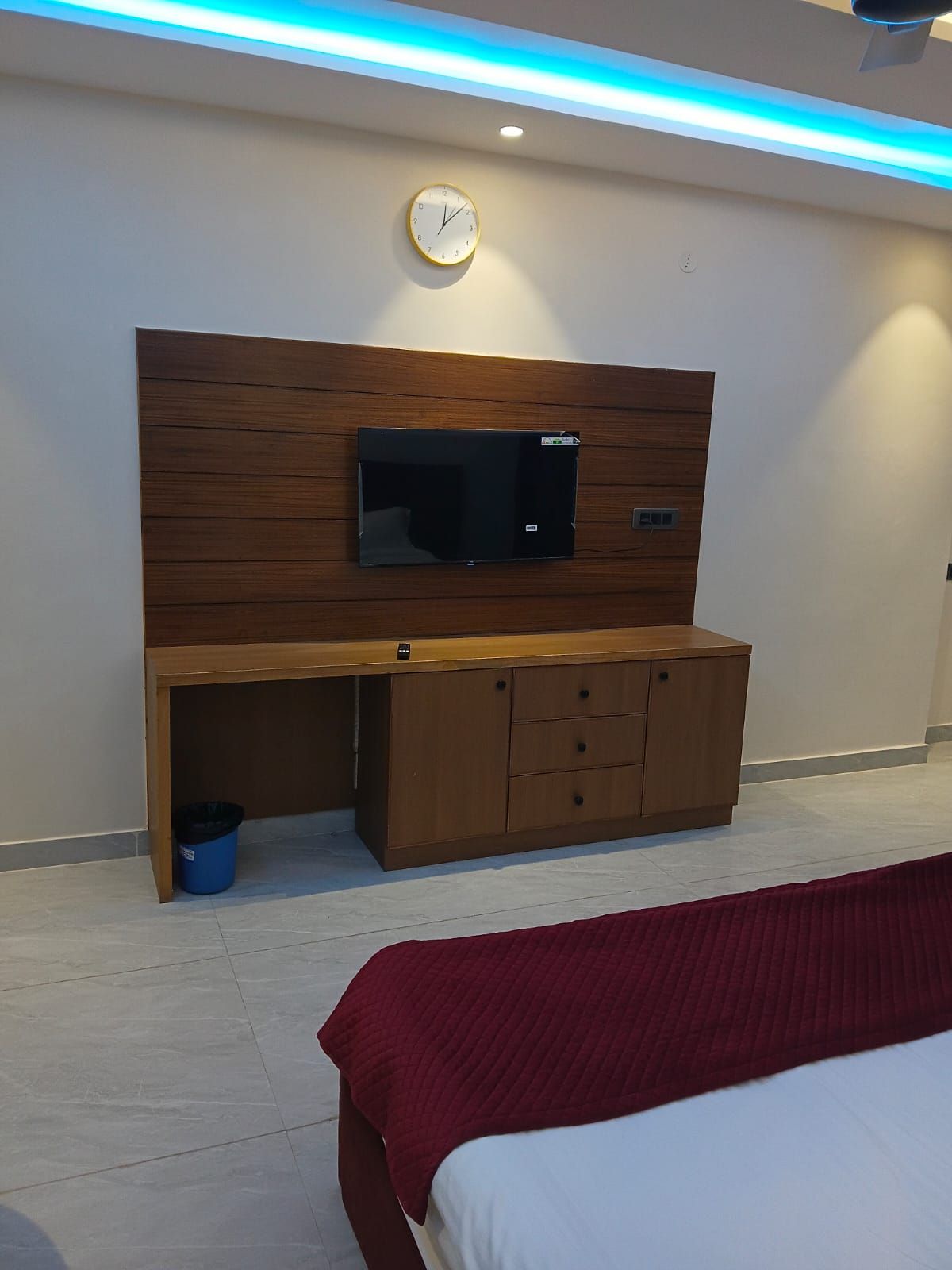 Una habitación de hotel con una cama, un escritorio de madera con un televisor y un reloj en la pared.