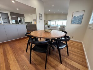 A modern kitchen with a dining area featuring a round wooden table and black chairs. - Love Street by HAUS · 4-Bedroom Kiama Home with Lift, Dog-Friendly (Kiama)