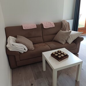 Een bruine bank met een witte tafel ervoor, een plaid en een spel.