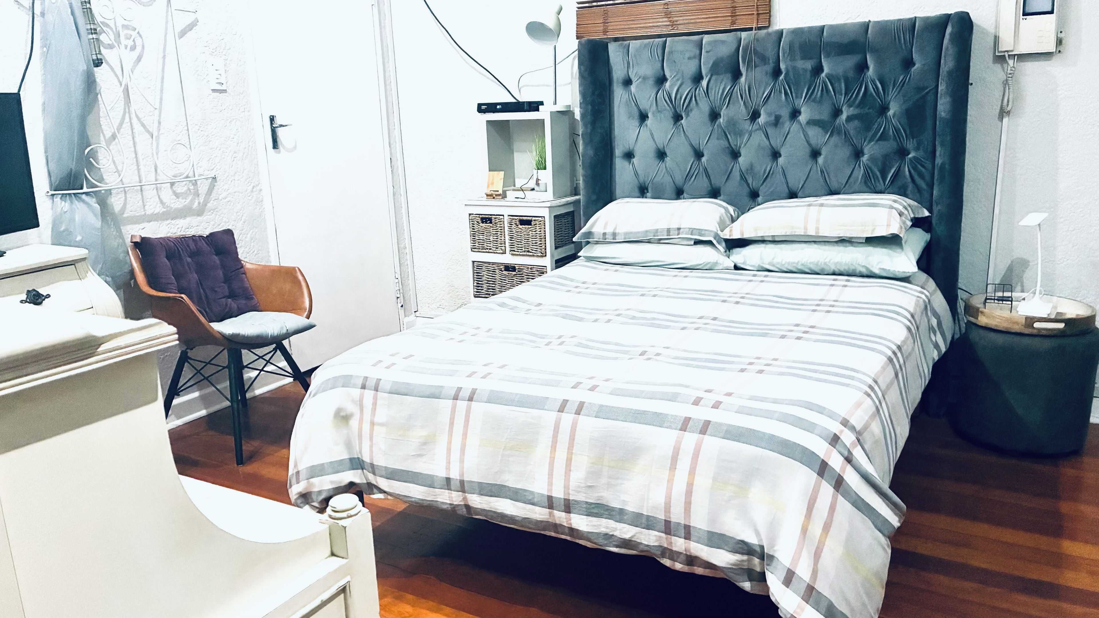 A bedroom with a bed, a chair, a bedside table, a lamp, and a wall-mounted phone.