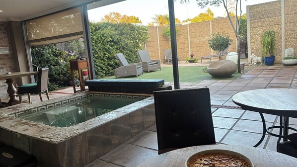 A pool area with a hot tub, lounge chairs, and a table.
