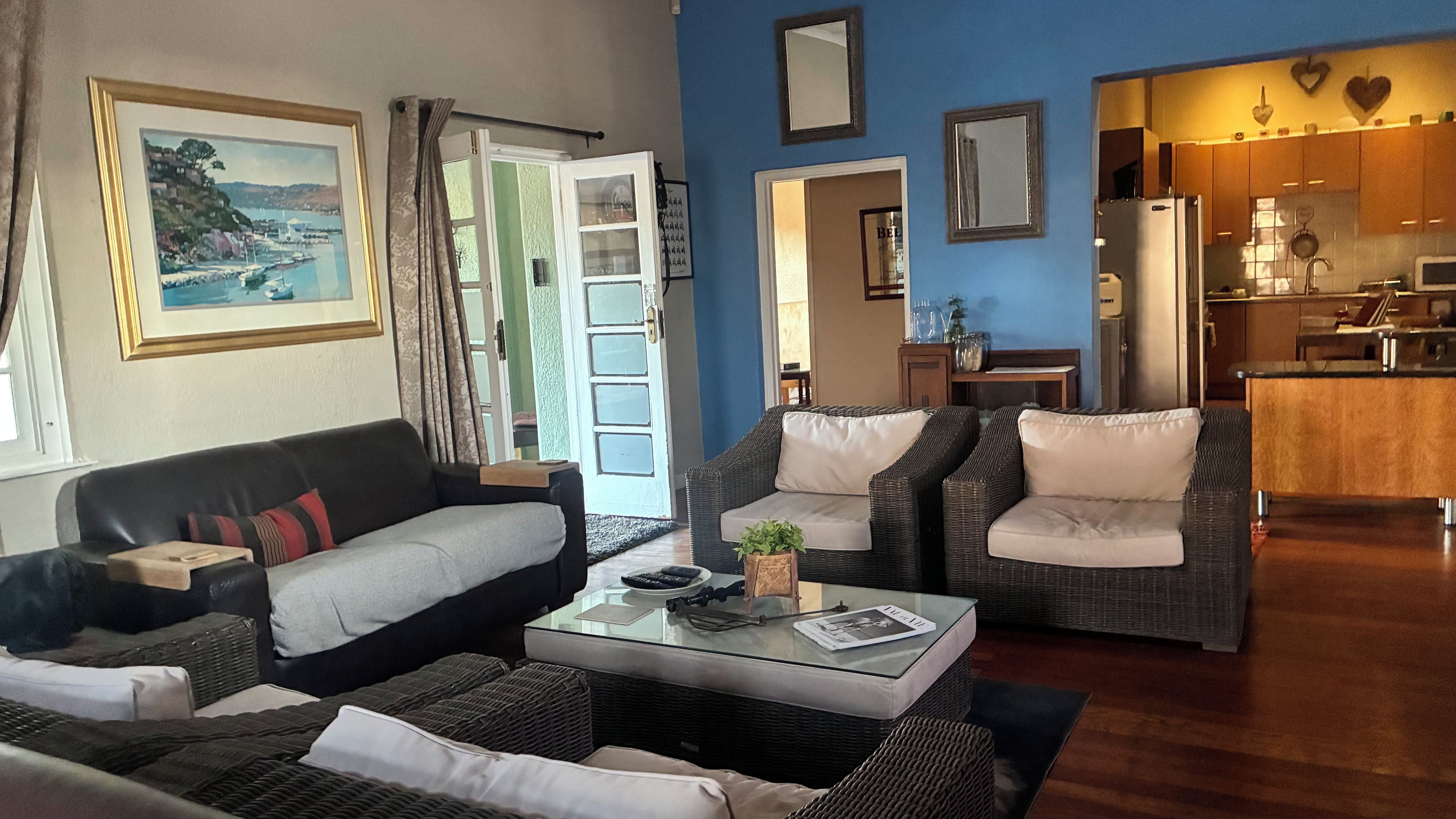 A living room with a sofa, two armchairs, a coffee table, and a view of the kitchen.