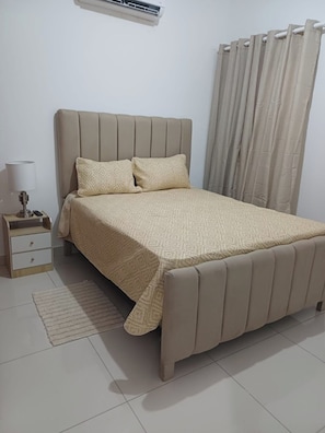 Une chambre à coucher avec un lit, une table de chevet, une lampe et des rideaux.