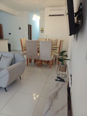 A modern living room with a grey sofa, a dining table with chairs, a potted plant, and a mounted television. - Sunset: 3 Queen Bedrooms, Pool & Gym, Beach Across the Street (Puerto Plata)