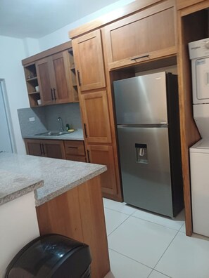 A kitchen with wooden cabinets, a stainless steel refrigerator, and a sink. - Sunset: 3 Queen Bedrooms, Pool & Gym, Beach Across the Street (Puerto Plata)