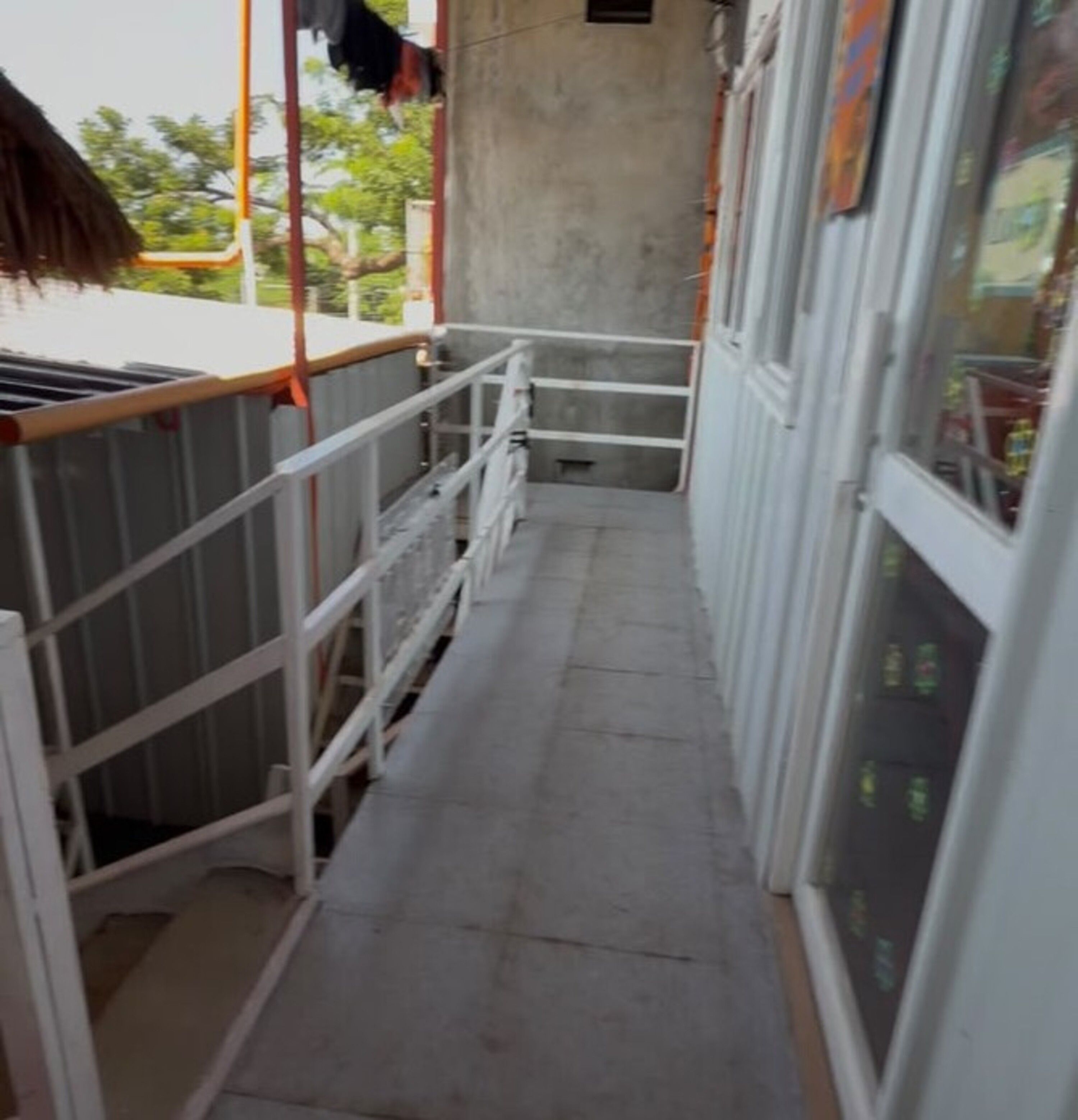 Un estrecho pasillo con barandillas de metal, suelo de concreto y vistas al exterior a través de una ventana.