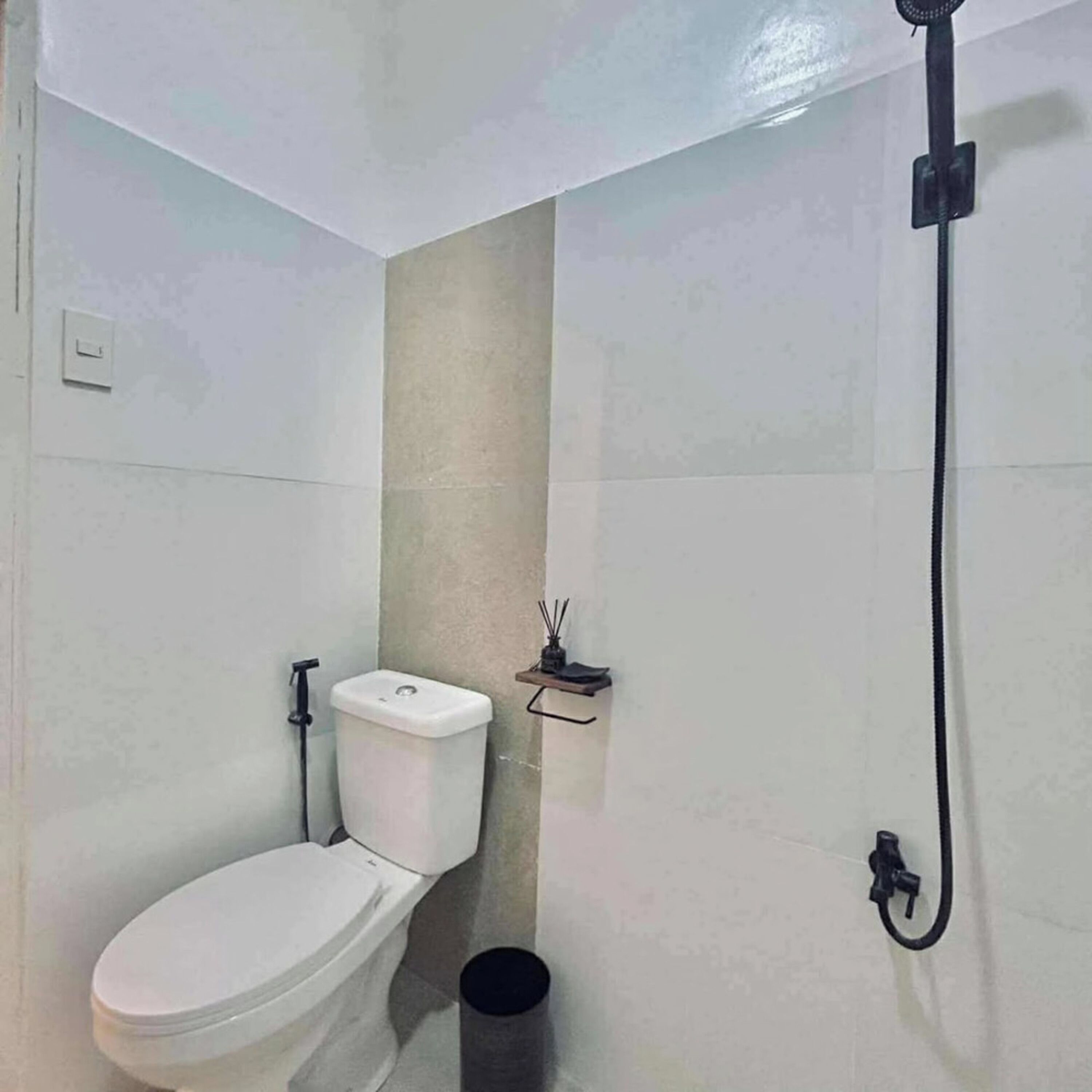 A small bathroom with a toilet, a shower, and a waste bin.