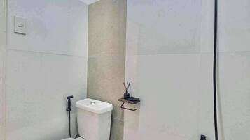 A small bathroom with a toilet, a shower, and a waste bin.