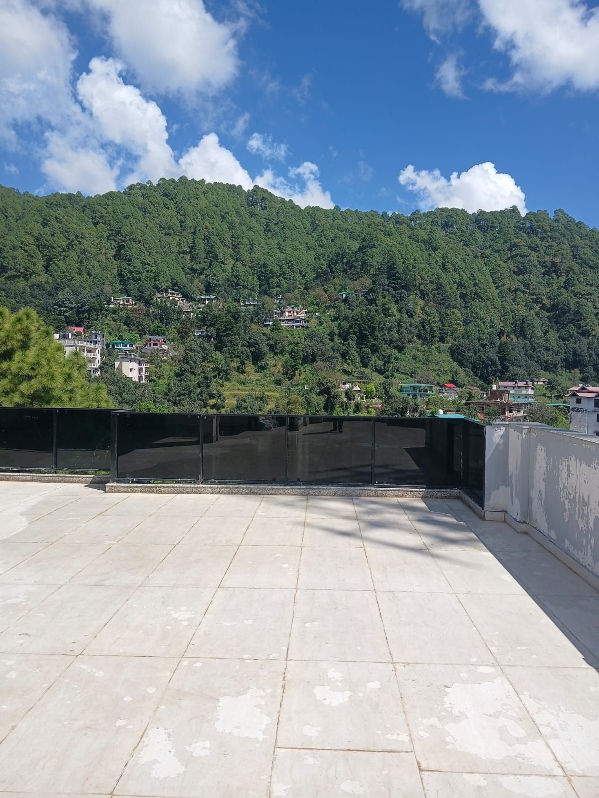 A rooftop terrace with a view of a densely forested hillside.