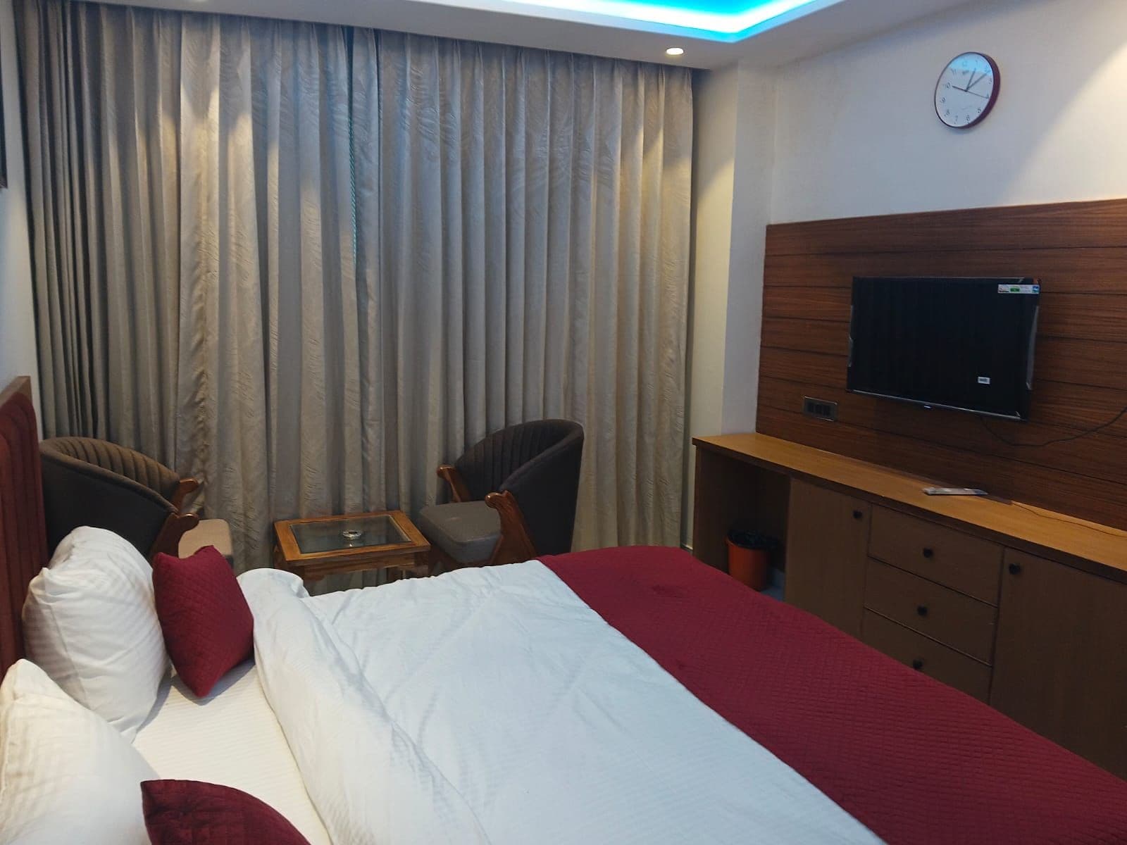 A hotel room with a bed, two armchairs, a small table, a TV, and a wooden cabinet.