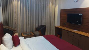 A hotel room with a bed, two armchairs, a small table, a TV, and a wooden cabinet.
