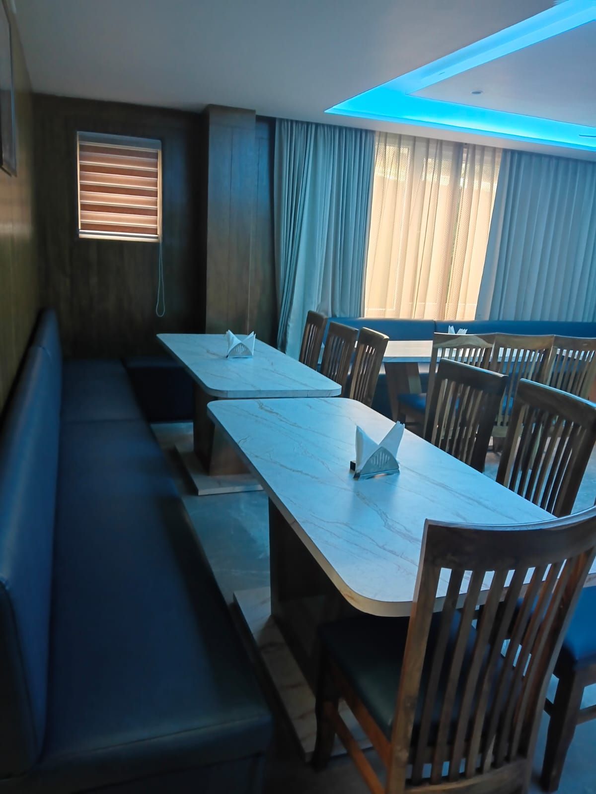 A dining area with a long table and benches, a window with blinds, and a ceiling with a skylight.