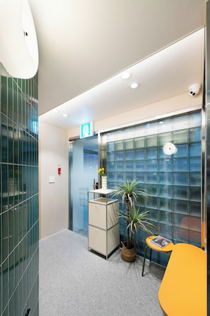 A modern lobby with a reception desk, a potted plant, a glass wall, and a small table with a magazine. - MING STAY Gangnam (Seoul)
