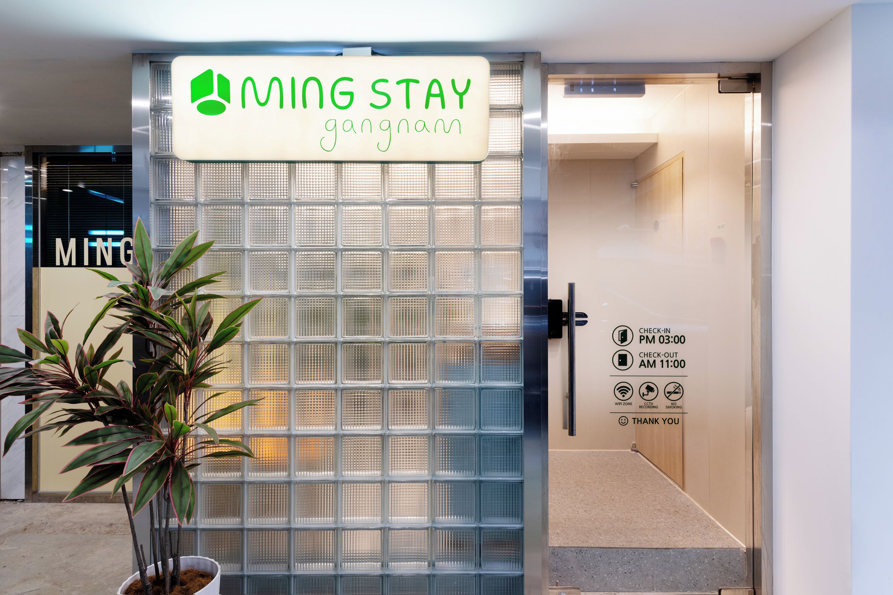 Una entrada con puerta protegida a una propiedad llamada 'MING STAY', con un cartel que indica registro de entrada a las 3:00 PM y salida a las 11:00 AM.
