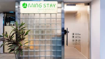 Una entrada con puerta protegida a una propiedad llamada 'MING STAY', con un cartel que indica registro de entrada a las 3:00 PM y salida a las 11:00 AM.