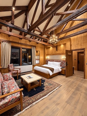 A spacious room with a large bed, a sitting area with a sofa and armchair, a wooden floor, and exposed wooden beams on the ceiling. - House of Khazir (Gulmarg)