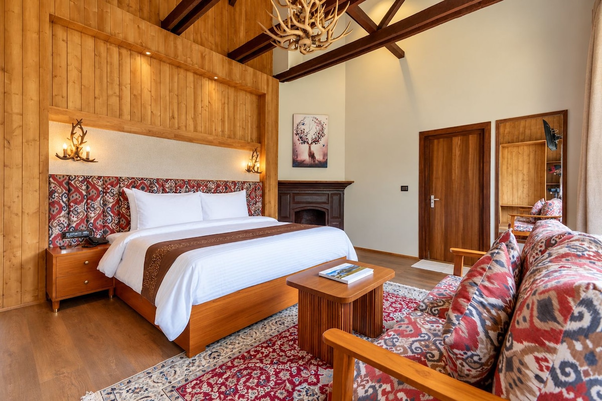 A bedroom with a wooden headboard, a bed, a nightstand, a bedside table, a fireplace, a sofa, and a patterned rug.