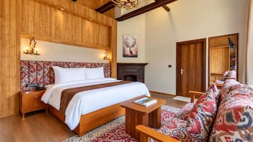 Quarto com cabeceira de madeira, cama, mesa de cabeceira, lareira, sofá e tapete estampado.