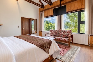 A bedroom with a large bed, a wooden-framed window, a sofa, and a view of greenery outside. - House of Khazir (Gulmarg)