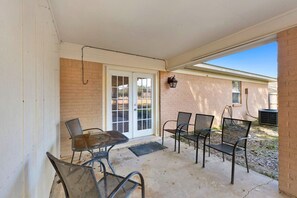 A covered patio with a table and chairs, a door leading to a garage, and a brick wall. - Flint Ridge (Mobile)