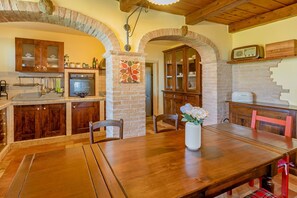 A rustic kitchen with wooden cabinets, a stone archway, and a dining table with chairs. - Villa Stefano by Anita Villas (Campofilone)