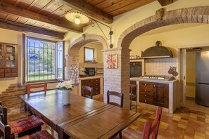 A rustic kitchen with a wooden table, chairs, and a stone archway. - Villa Stefano by Anita Villas (Campofilone)