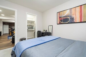 Un dormitorio con cama, un escritorio con silla, un espejo y un cuadro en la pared.
