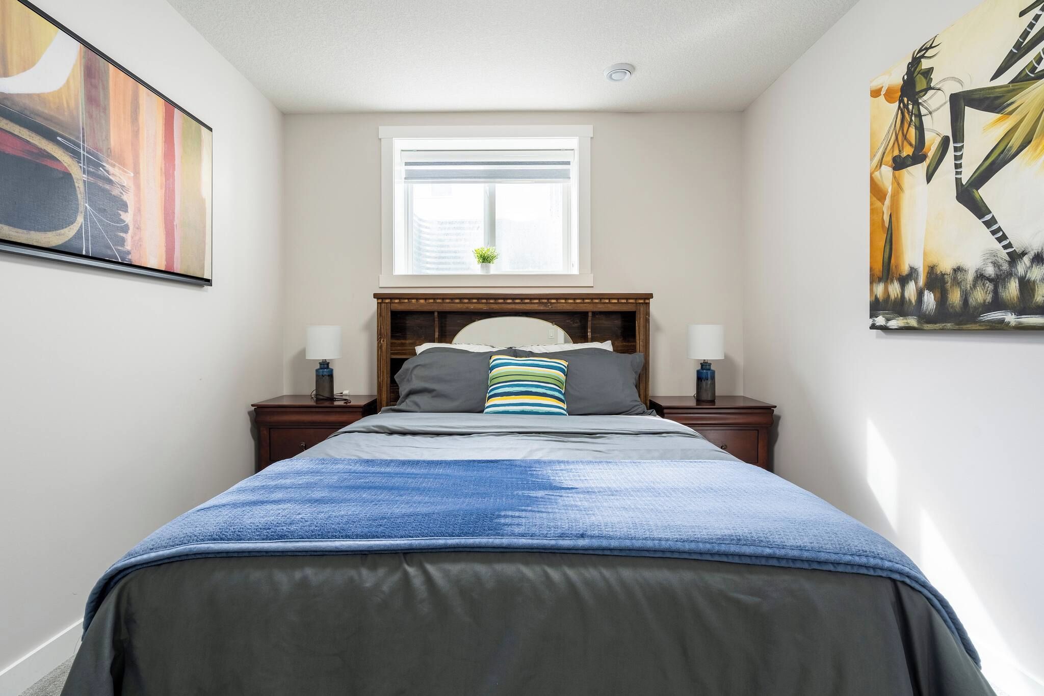 A bedroom with a bed, two bedside tables, a window, and artwork on the walls.