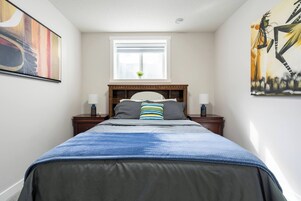 Un dormitorio con cama, dos mesitas de noche, una ventana y obras de arte en las paredes.
