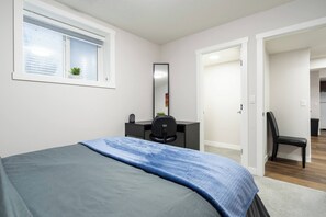 A bedroom with a bed, a desk, a chair, a mirror, and a window with blinds. - Plush Suite Pet Friendly 326 Mbps Wi-fi (Airdrie)