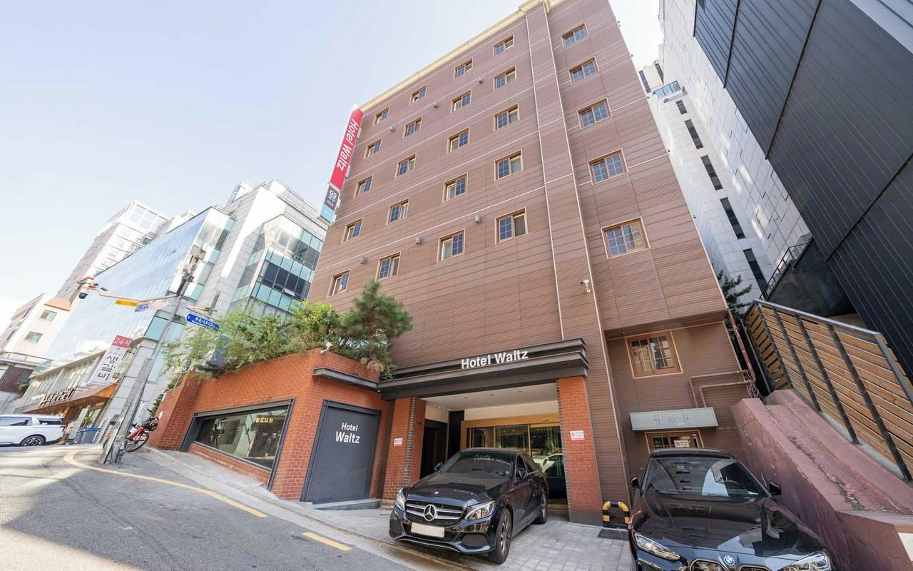 Un hotel de varios pisos con una entrada destacada, una zona de estacionamiento y una fachada de edificio moderna.