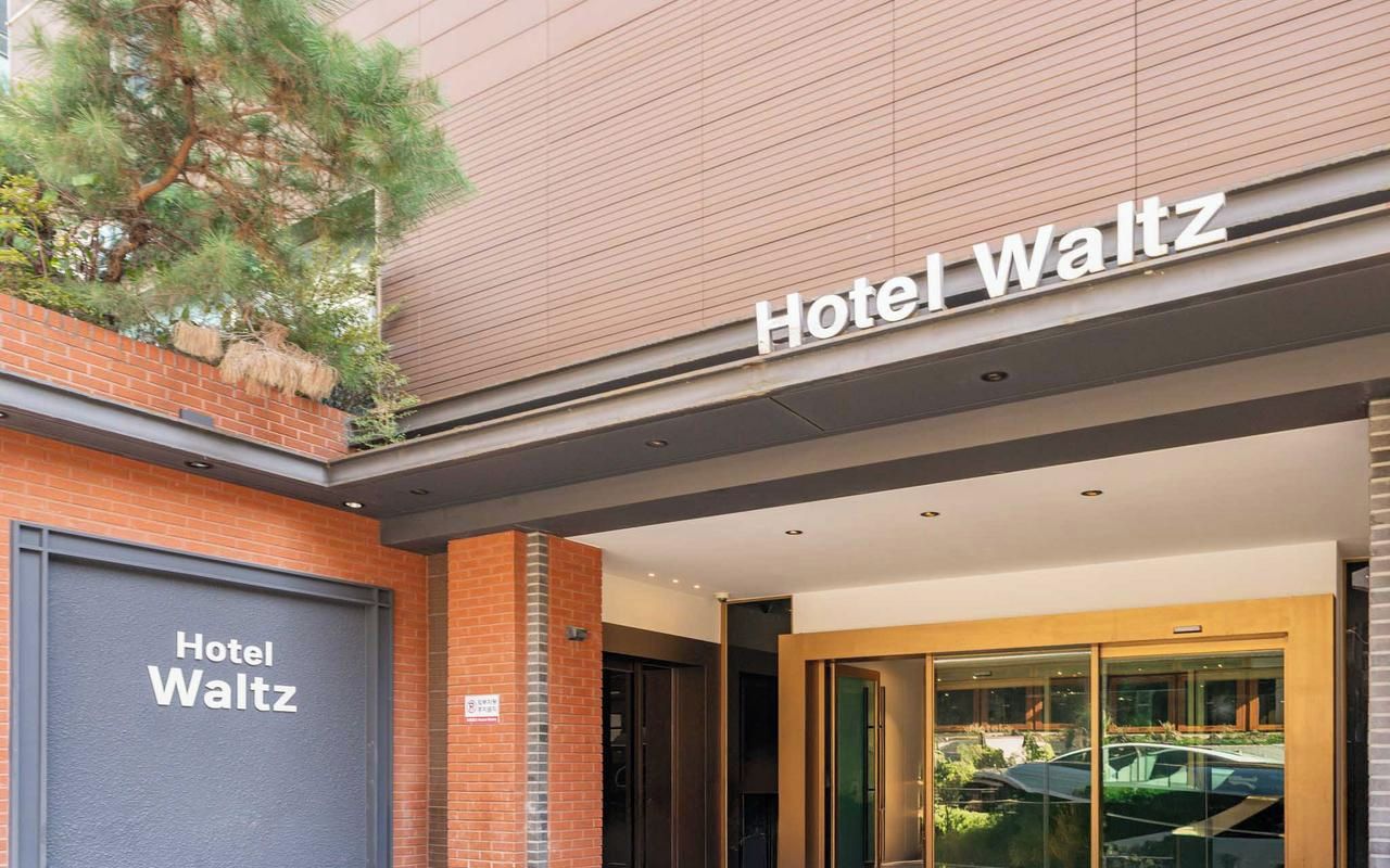 El exterior del Hotel Waltz, con una entrada destacada, una puerta de garaje visible y una vista clara del área de estacionamiento.