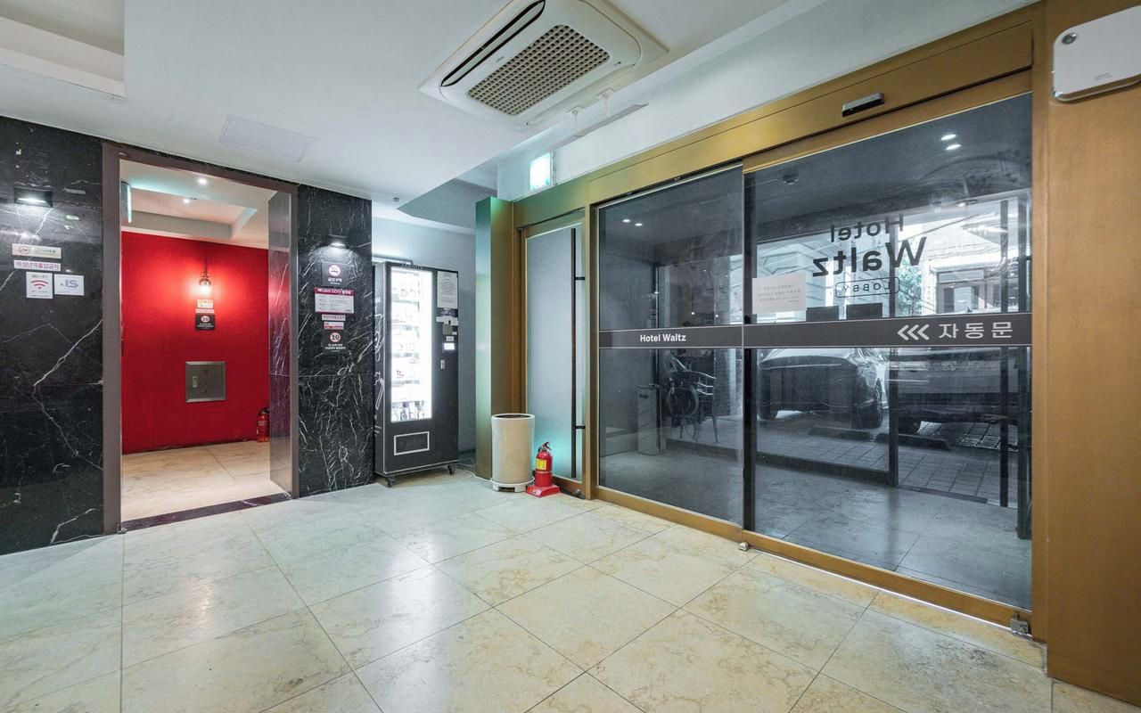 Eine Hotellobby mit roter Wand, einem Feuerlöscher und einer Glastür zum Parkplatz.
