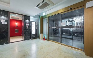 Vestíbulo de hotel con una pared roja, un extintor y una puerta de vidrio que da al estacionamiento.