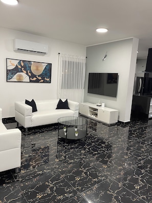 A modern living room with a sectional sofa, a glass coffee table, a flat-screen TV, and a decorative wall piece. - Villa del Carmen 4BR Pool Villa, 3-Min Walk to Beach & River (Cabrera)
