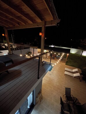 An outdoor patio area with a wooden deck, seating, and ambient lighting. - Villa del Carmen 4BR Pool Villa, 3-Min Walk to Beach & River (Cabrera)