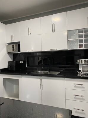A modern kitchen with white cabinets, a black countertop, a microwave, a coffee maker, and a wine glass holder. - Villa del Carmen 4BR Pool Villa, 3-Min Walk to Beach & River (Cabrera)