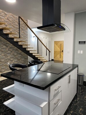 A modern kitchen with a black countertop, white cabinets, and a wooden staircase. - Villa del Carmen 4BR Pool Villa, 3-Min Walk to Beach & River (Cabrera)