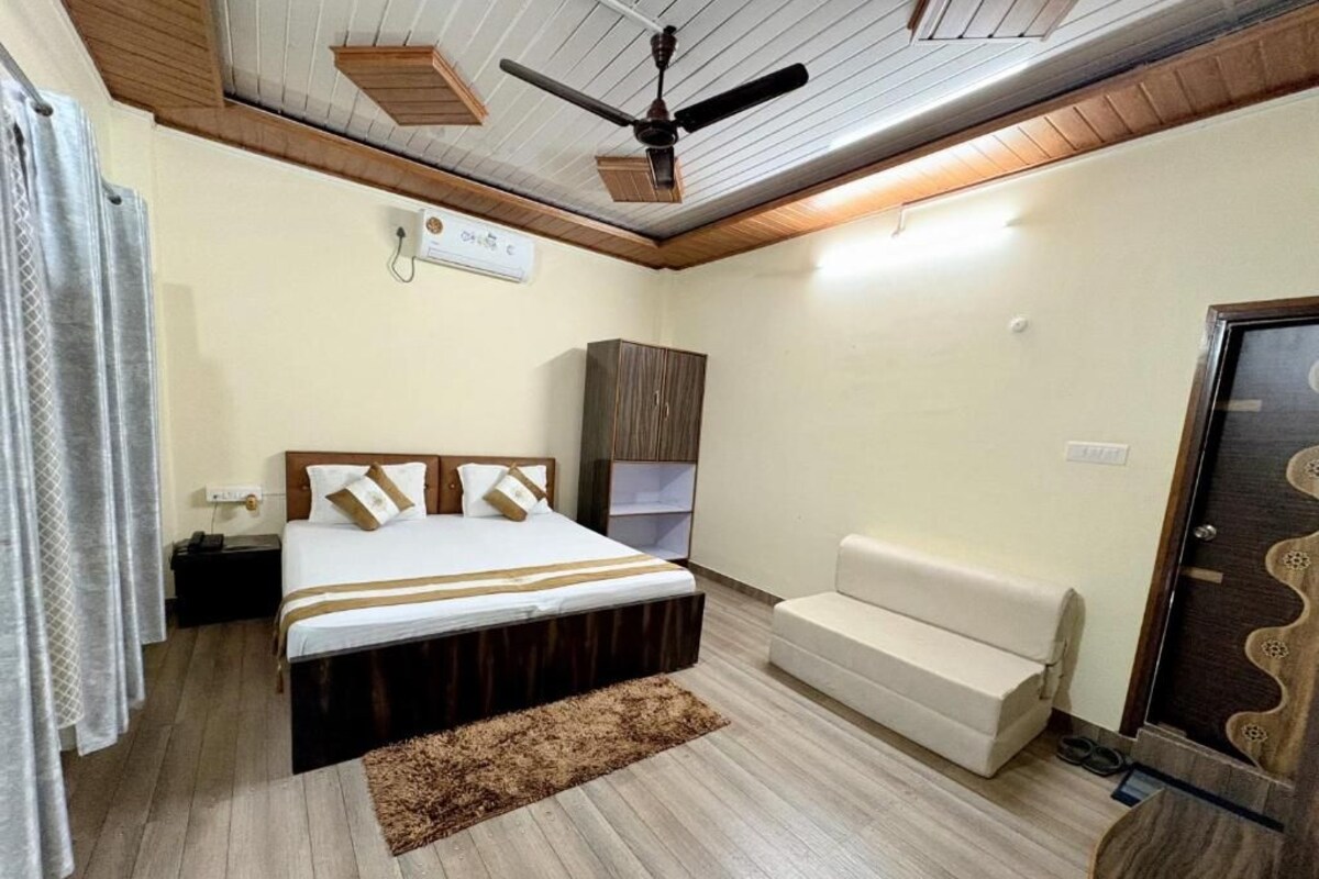 Quarto com cama, sofá branco, ventoinha no teto e armário de madeira.