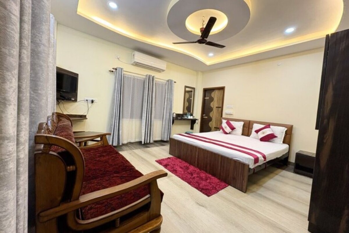 Quarto de hotel com cama, escrivaninha, cadeira, ventilador de teto e televisão.