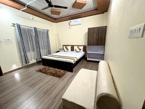 Quarto com cama, guarda-roupa, um banquinho e ventoinha no teto.