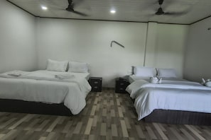 Habitació d'hotel amb dos llits, un sòl de parquet de fusta, ventiladors de sostre i una paret blanca.